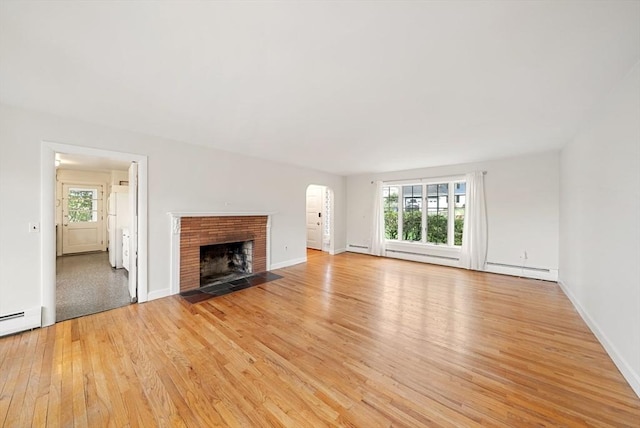 unfurnished living room with light wood-type flooring, arched walkways, healthy amount of natural light, and a brick fireplace