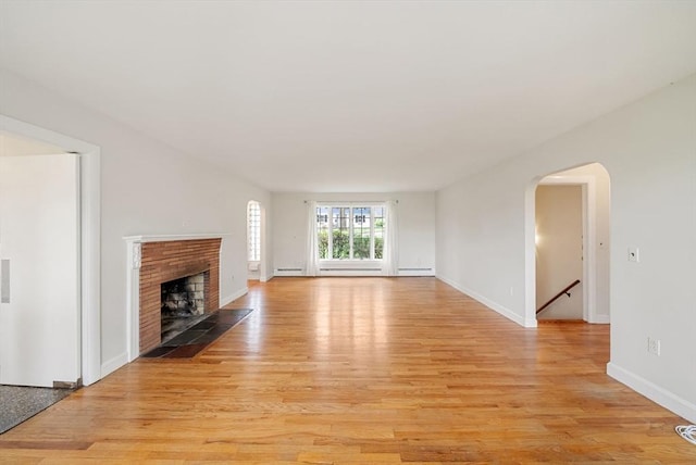 unfurnished living room featuring light wood-style floors, a brick fireplace, arched walkways, and baseboards