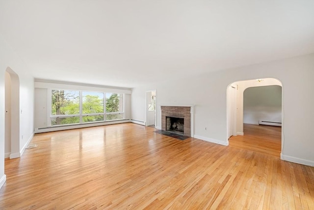 unfurnished living room with a baseboard radiator, arched walkways, light wood-style flooring, a fireplace, and baseboards
