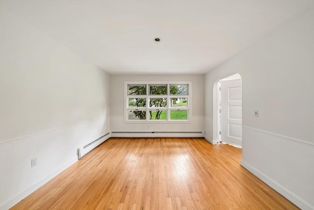 spare room featuring light wood-style flooring, arched walkways, and a baseboard radiator