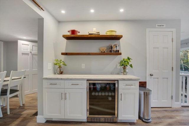 bar featuring recessed lighting, beverage cooler, a bar, and light wood finished floors