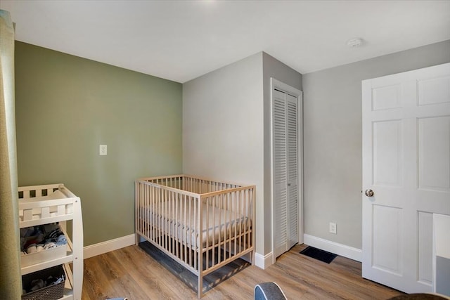 bedroom with a nursery area, a closet, baseboards, and wood finished floors