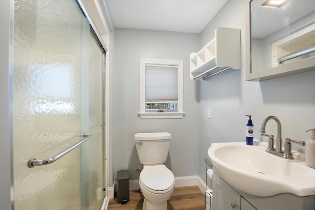 bathroom with toilet, wood finished floors, vanity, baseboards, and a shower stall