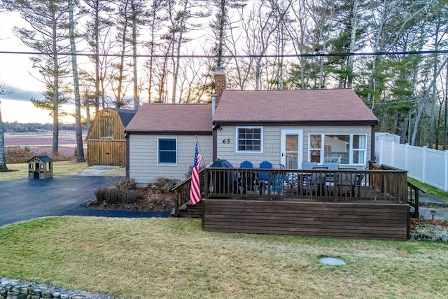 view of front of home featuring roof with shingles, a chimney, a front yard, fence, and a wooden deck