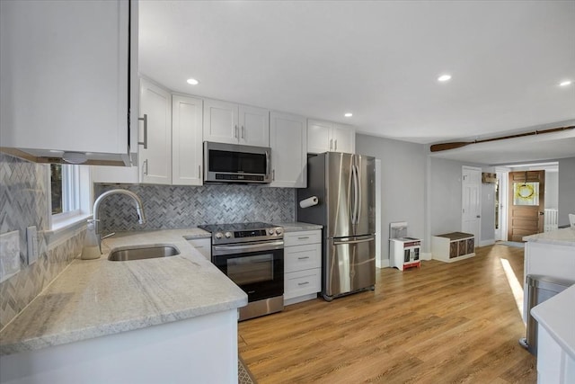 kitchen featuring decorative backsplash, stainless steel appliances, light wood-style floors, white cabinetry, and a sink