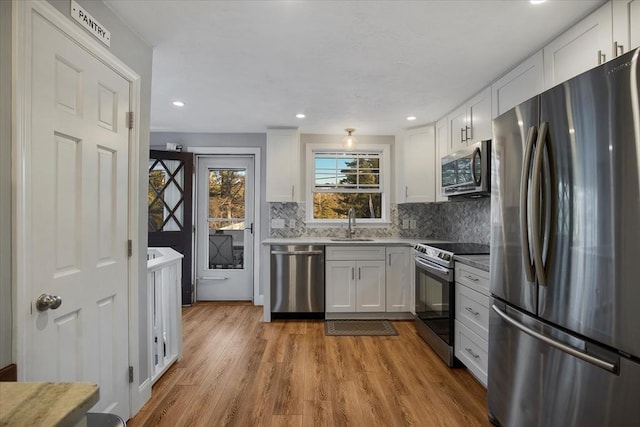 kitchen featuring stainless steel appliances, light wood finished floors, decorative backsplash, and white cabinets