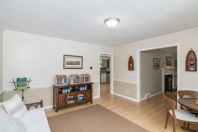 living room with crown molding, a fireplace, visible vents, and light wood-style floors