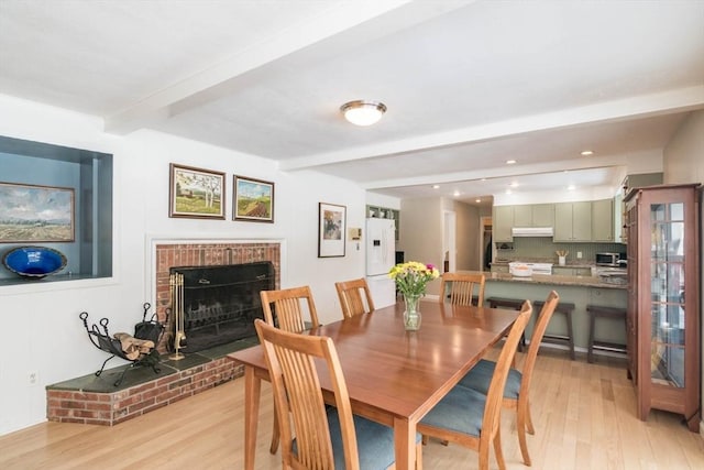 dining area featuring recessed lighting, a fireplace, beamed ceiling, and light wood finished floors