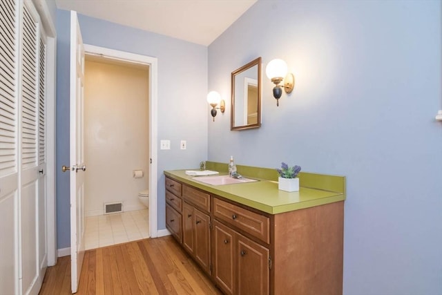 bathroom with a closet, visible vents, toilet, vanity, and wood finished floors