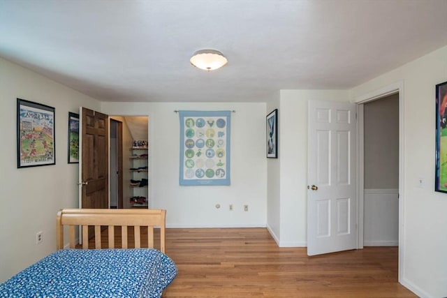 bedroom with a walk in closet, light wood-style flooring, and baseboards