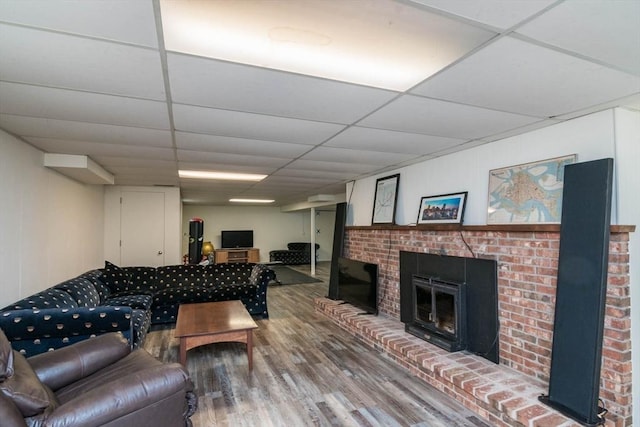 living room featuring a drop ceiling, a brick fireplace, and wood finished floors