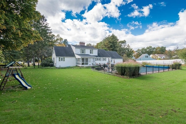 back of house with a lawn, a fenced in pool, a sunroom, a chimney, and a playground