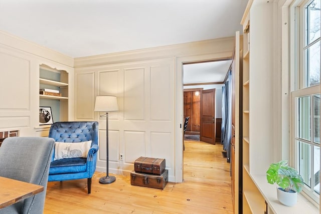 sitting room featuring crown molding, built in features, and light hardwood / wood-style floors