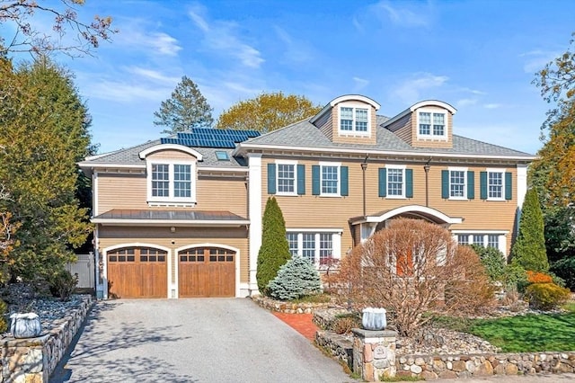 25 Wedgemere Ave, Winchester, MA 01890 - view of front of house featuring asphalt driveway, an attached garage, roof mounted solar panels, and roof with shingles