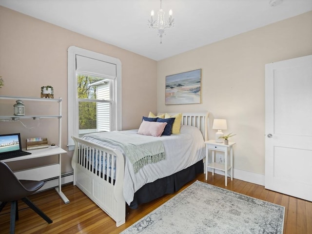 bedroom with wood-type flooring, a baseboard heating unit, baseboards, and an inviting chandelier