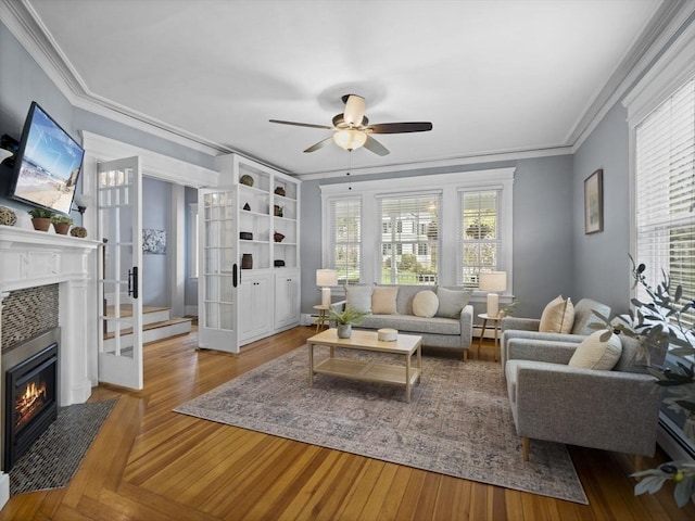 living room with a healthy amount of sunlight, ceiling fan, a tile fireplace, and crown molding