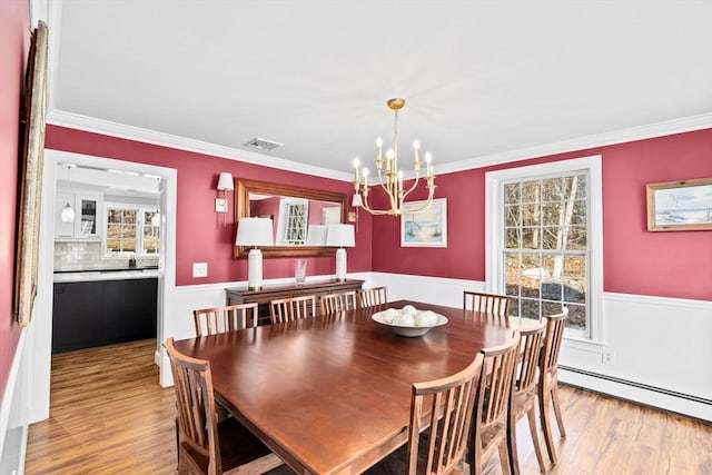 dining area with a wainscoted wall, baseboard heating, wood finished floors, and crown molding