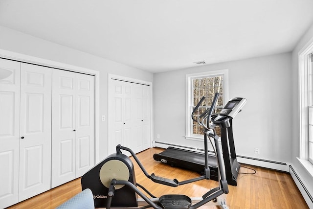 workout area featuring plenty of natural light, light wood-style flooring, visible vents, and a baseboard heating unit