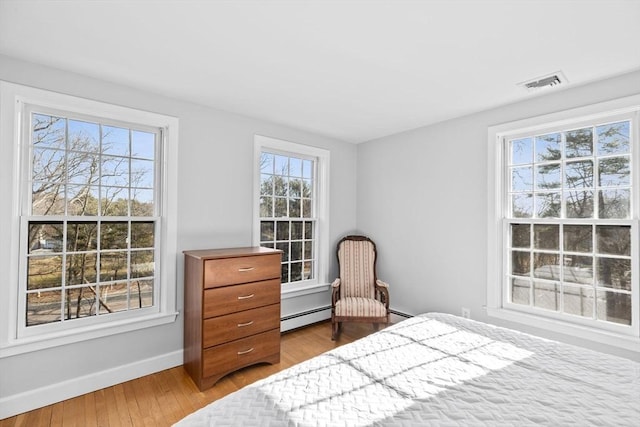 bedroom with baseboard heating, wood finished floors, visible vents, and baseboards