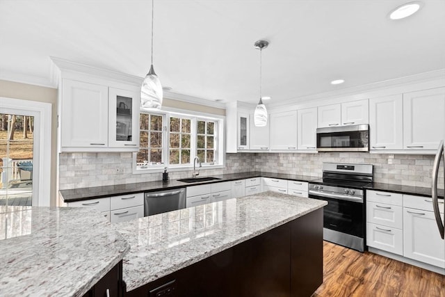 kitchen with stainless steel appliances, a sink, white cabinets, ornamental molding, and glass insert cabinets