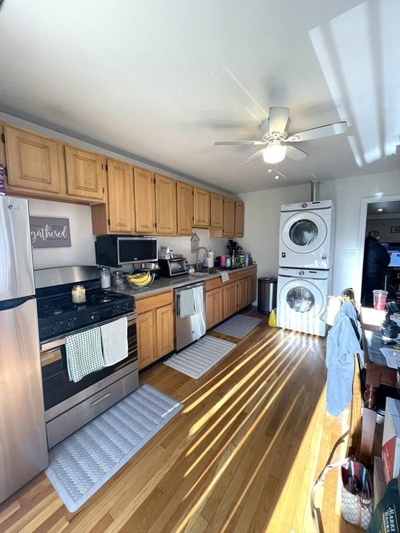 kitchen featuring appliances with stainless steel finishes, stacked washer and dryer, light wood-type flooring, sink, and ceiling fan