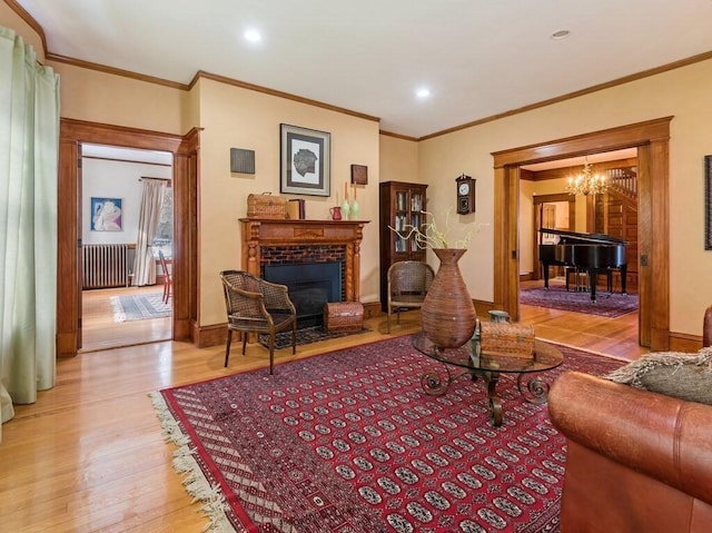 living room featuring a notable chandelier, crown molding, a fireplace, and light wood-type flooring