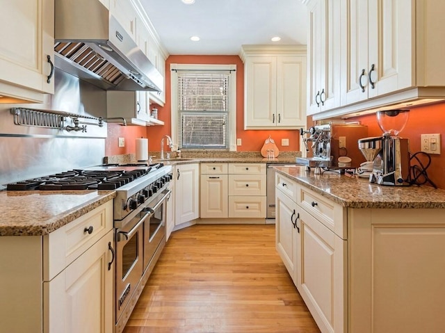 kitchen with sink, light hardwood / wood-style flooring, light stone countertops, exhaust hood, and range with two ovens