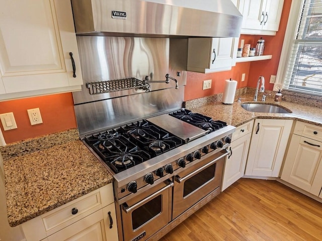 kitchen featuring sink, light hardwood / wood-style flooring, light stone counters, and wall chimney exhaust hood