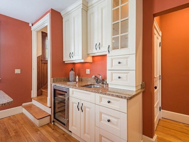 kitchen with sink, white cabinetry, light hardwood / wood-style flooring, beverage cooler, and light stone countertops