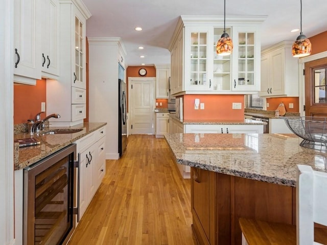 kitchen featuring sink, beverage cooler, hanging light fixtures, light stone counters, and black fridge