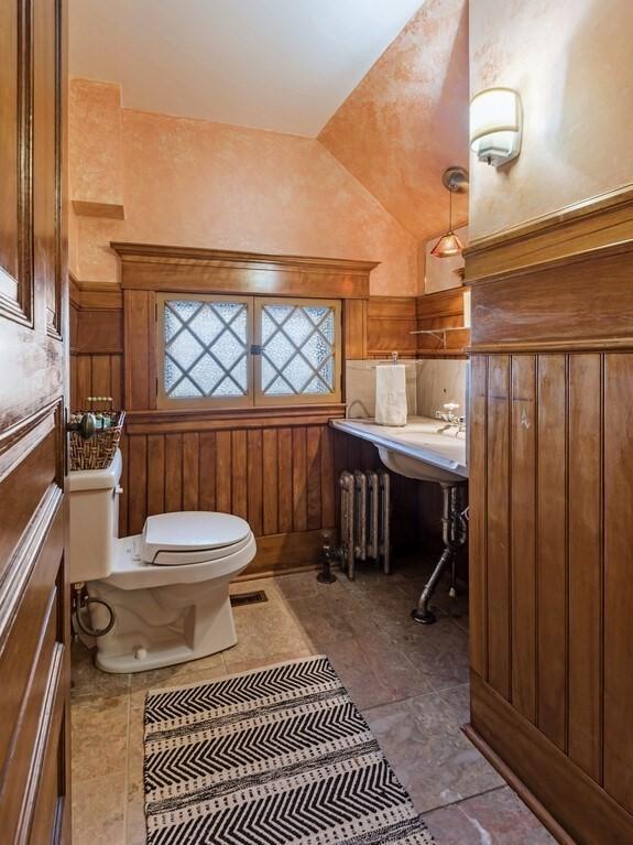 bathroom featuring lofted ceiling, radiator, wooden walls, and toilet