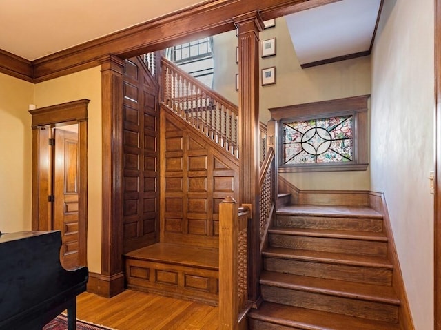 stairs featuring hardwood / wood-style floors, a wealth of natural light, decorative columns, and ornamental molding