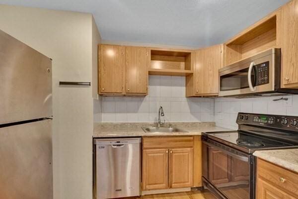 kitchen with stainless steel appliances, open shelves, a sink, and light countertops