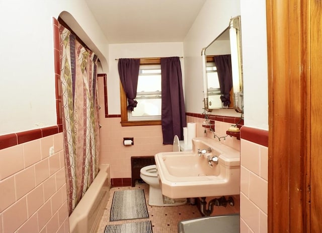 full bathroom with toilet, tile walls, a sink, and wainscoting