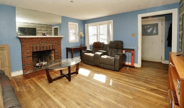 living area featuring baseboard heating, a fireplace, baseboards, and wood finished floors