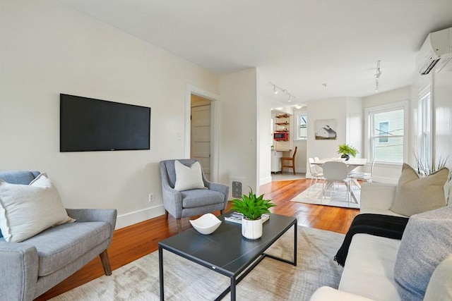living room with baseboards, rail lighting, light wood-style floors, and a wall mounted AC