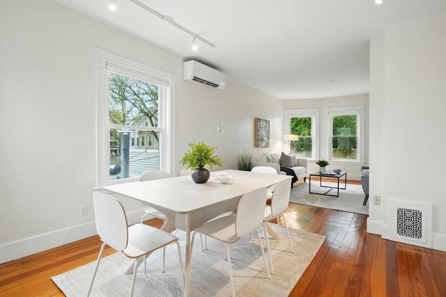 dining space with an AC wall unit, hardwood / wood-style flooring, baseboards, and track lighting