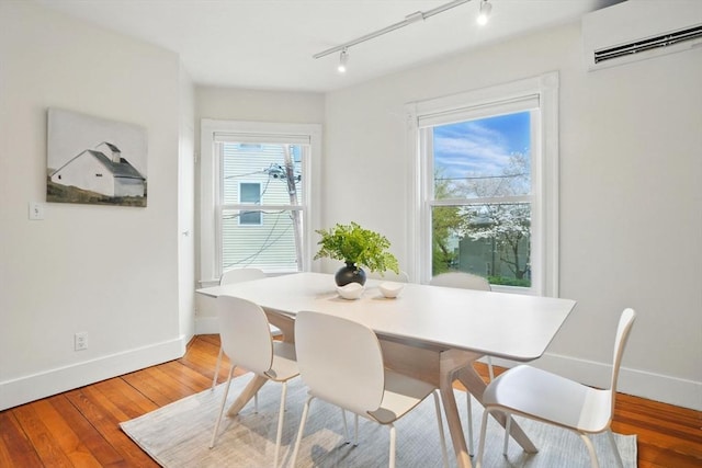 dining area featuring a wall mounted AC, rail lighting, baseboards, and light wood finished floors