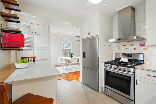 kitchen with appliances with stainless steel finishes, wall chimney exhaust hood, light tile patterned flooring, white cabinetry, and tasteful backsplash