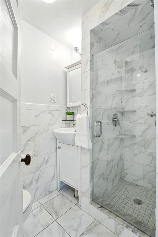 full bath featuring a stall shower, vanity, marble finish flooring, tile walls, and wainscoting