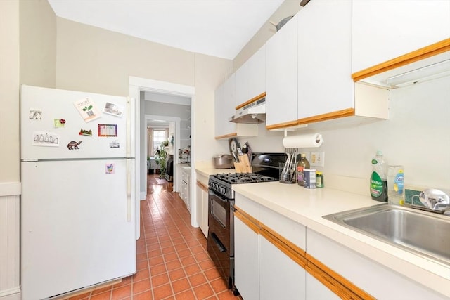 kitchen with freestanding refrigerator, black gas range, under cabinet range hood, a sink, and tile patterned flooring