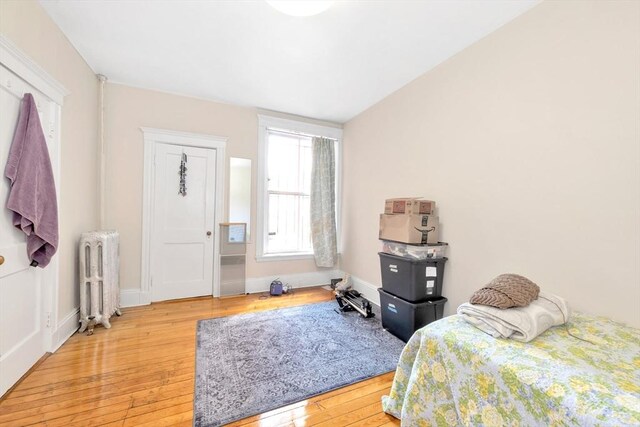 bedroom with radiator heating unit, wood-type flooring, and baseboards