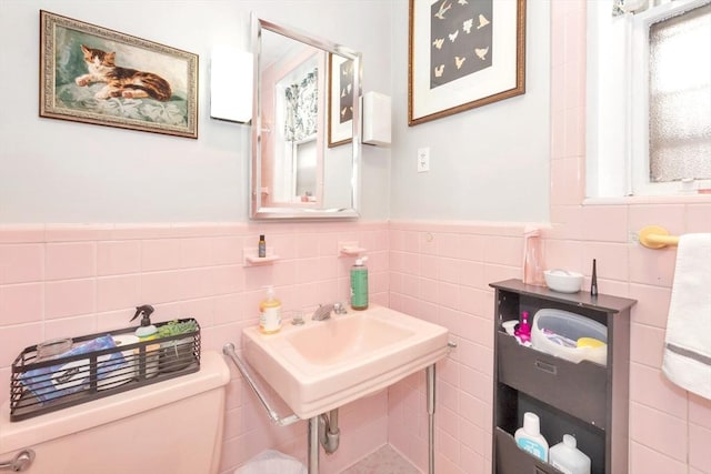 half bath featuring tile walls, a wainscoted wall, toilet, and a sink