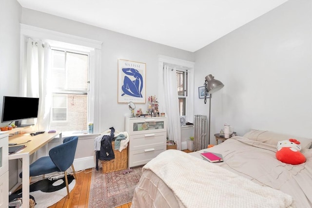 bedroom with radiator, wood finished floors, a desk, and baseboards