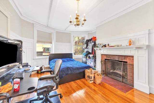 bedroom with a chandelier, wood finished floors, a brick fireplace, a desk, and crown molding