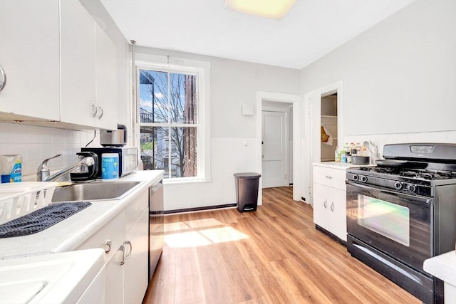 kitchen featuring black gas range oven, white cabinetry, light countertops, light wood-type flooring, and tasteful backsplash