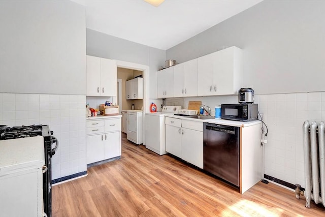 kitchen featuring black appliances, separate washer and dryer, radiator, tile walls, and a sink