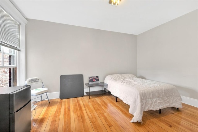bedroom featuring baseboards, freestanding refrigerator, and wood-type flooring
