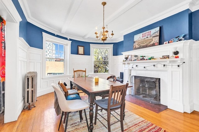 dining room featuring radiator, light wood finished floors, a fireplace with flush hearth, a chandelier, and beamed ceiling