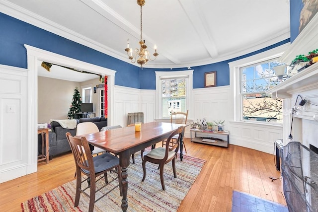 dining room with a decorative wall, light wood finished floors, a chandelier, wainscoting, and beamed ceiling